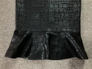 Detail view of the crocodile texture and ruffled fishtail hem on the black bandage dress
