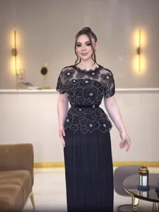 Elegant black lace floral dress with pleated skirt worn by a model in a luxury interior.