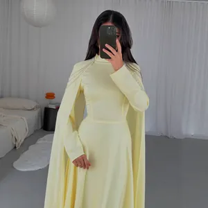 Elegant detail showing a yellow high-neck maxi dress with cape sleeves and fringe accents