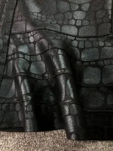 Macro detail of metallic crocodile pattern on a black bandage dress material.