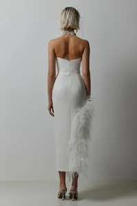 Back view of a white strapless midi dress with luxurious ostrich feather slit detail.