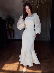 Abito lungo bianco elegante con applicazioni floreali e maniche a sbuffo velate.