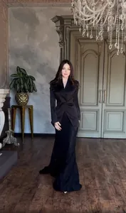 Elegant model wearing a black tailored blazer and long skirt set in a grand interior.