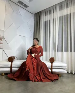 Ganzkörperansicht einer eleganten, rostroten, langärmeligen Abendrobe in sitzender Pose.