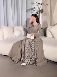 Elegantes taupefarbenes Maxikleid mit Faltenrock, präsentiert von einem Model auf einem Sofa