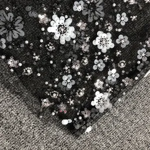 Close-up of intricate white floral sequins and silver beadwork on black mesh fabric