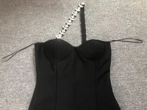 Detail view of the heavy rhinestone embellished strap on a black one-shoulder bandage dress