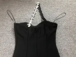 Detail of sparkling rhinestone chain shoulder strap on elegant black bandage dress