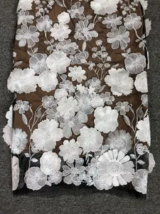 Close-up detail of white floral embroidery on brown mesh fabric for elegant evening dress