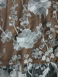 Close-up showing the intricate white 3D floral embroidery on a brown evening gown