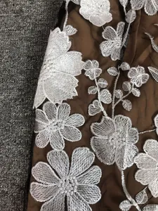 Close-up view of white floral embroidery on a brown mesh party dress fabric.
