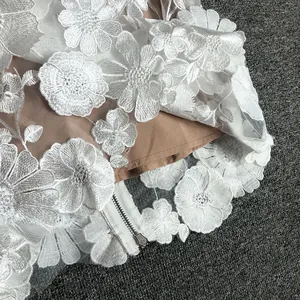 Close-up of white 3D floral lace embroidery detail and zipper on an elegant evening dress.