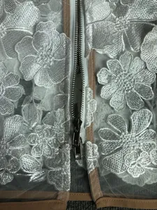 Detailed macro view of white 3D floral embroidery and silver zipper on dress.