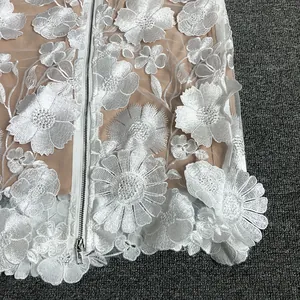 Detailed macro view showing intricate 3D white floral embroidery on elegant lace dress