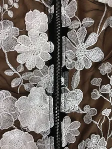 Detailed close-up of white floral embroidery on brown mesh dress with black zipper