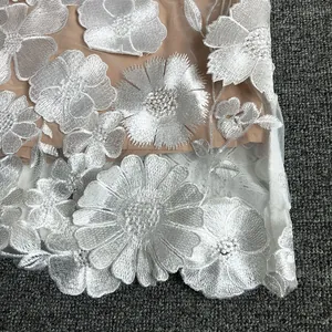 Close-up of intricate 3D white floral lace embroidery on an elegant evening gown fabric.