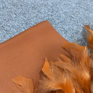 Detailaufnahme eines orangefarbenen Bandagekleid-Stoffs mit elegantem Federbesatz und Rippenmuster