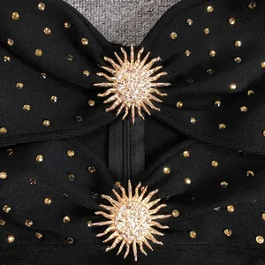 Detail of sun-shaped gold metal accessories on a black rhinestone bandage dress.