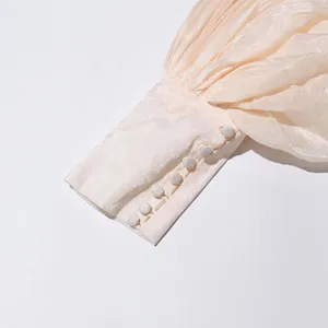 Gros plan du poignet bouffant plissé crème avec boutons recouverts de tissu sur une robe