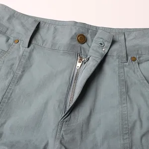 Dettaglio della cerniera metallica e del bottone su pantaloni cargo stile blu lavato.