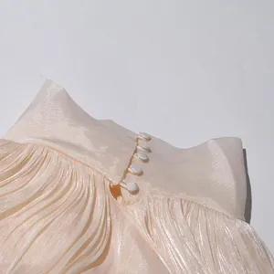 Gros plan d'une robe plissée champagne montrant la texture et les boutons élégants