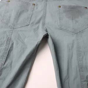 Dettaglio delle tasche posteriori e dei rivetti su pantaloni cargo svasati grigi invecchiati.