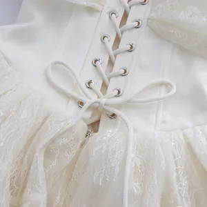 Detailansicht eines weißen Kleides mit Korsett-Schnürung und Spitzen-Mesh-Details.