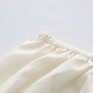 Nahaufnahme des elastischen, gefalteten Ausschnitts eines cremefarbenen Kleides.