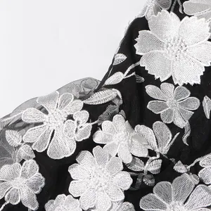 Detailed close-up view of exquisite white floral embroidery on premium black mesh fabric