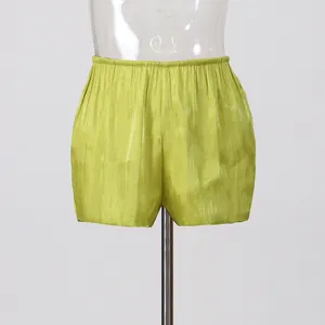 Close-up view of shiny lime green holiday style high-waisted shorts with pleated detail.