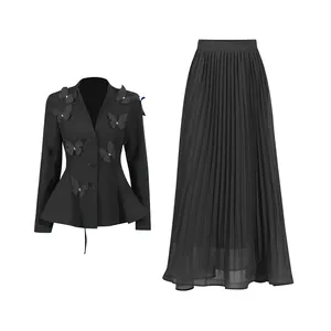 Détail d'un ensemble luxe noir avec blazer à papillons 3D et jupe longue plissée.