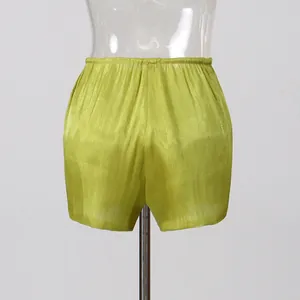 Detailed view of lime green pleated shimmer shorts with elastic waistband on mannequin