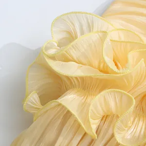 Close-up macro view of the yellow pleated fabric and tiered ruffle detail on a woman's dress.