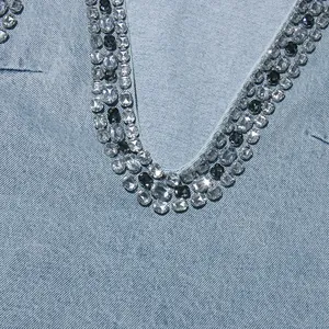 Dettaglio ravvicinato delle decorazioni in strass sullo scollo a V di un abito in denim