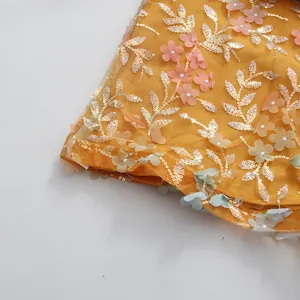 Gros plan détaillé d'une robe en maille jaune avec paillettes dorées et fleurs 3D colorées.