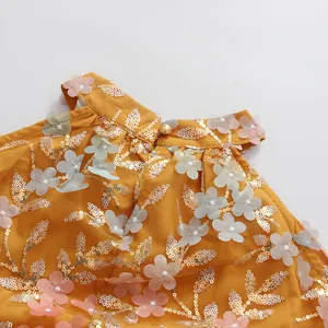 Détail des appliqués floraux 3D et des paillettes sur une robe jaune sans manches
