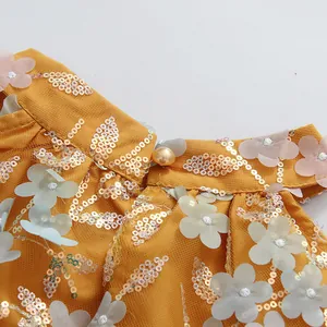 Gros plan détaillé d'une robe fleurie jaune avec paillettes dorées et bouton en perle élégant
