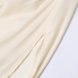 Détail du haut de la fente latérale élégante et du tissu soyeux de cette robe longue crème