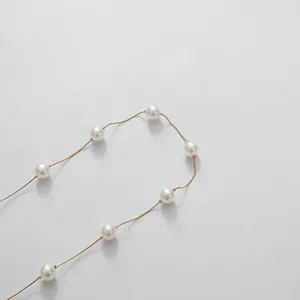 Détail en gros plan d'un collier en chaîne dorée minimaliste avec perles blanches.