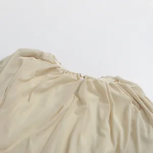 Close-up detail of pleated round neckline and pearl button on beige dress