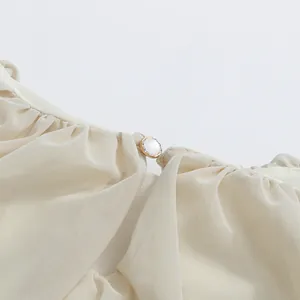 Detailed view of the exquisite pearl button closure on a cream pleated mesh dress