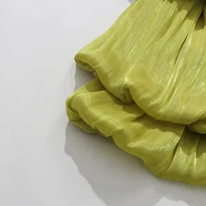Close-up of lime green pleated fabric texture with elegant sheen for resort dress detail