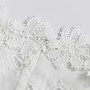 Primer plano de un vestido blanco con encaje bordado calado y una cremallera oculta.