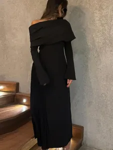 Elegante vestido largo negro con hombros descubiertos, escote asimétrico y manga larga.