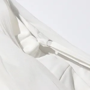 Detalle macro de chaqueta blanca con empalme de malla y tirante fino en el hombro.