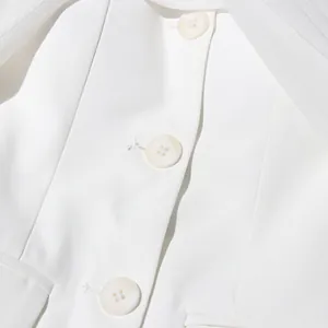 Primer plano de blazer blanco con botones de textura nácar y detalles de tul fino