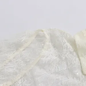 Detailansicht von weißer Blumenstickerei und glitzernden Pailletten auf einem Spitzenkleid.