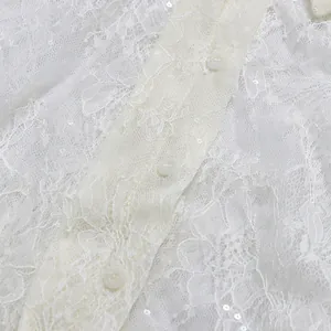 Detailansicht eines weißen Spitzenkleides mit floralem Muster und Glitzerpailletten