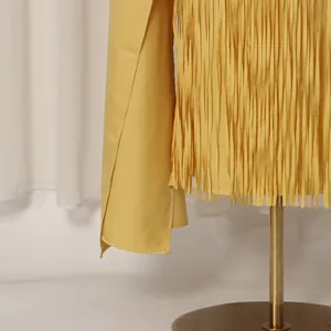 Close-up of elegant yellow dress featuring intricate fringe tassels and cape sleeve detail