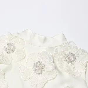 Gros plan d'une robe de soirée blanche avec des appliques florales 3D et perles.